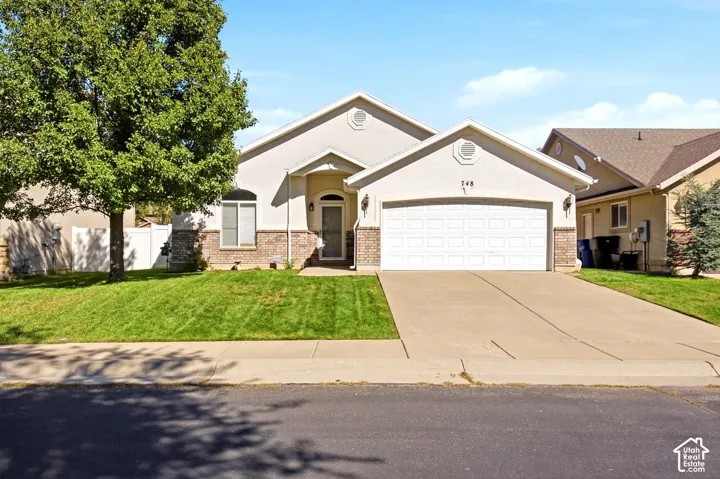Stucco exterior with brick detailing, arched entry, two-car garage, concrete driveway, and front lawn