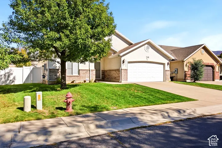 Stucco and brick facade with a two-car garage, concrete driveway, and front lawn