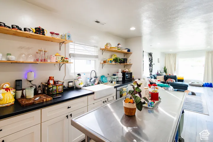 White shaker cabinetry with dark hardware and countertops, open shelving, farmhouse-style sink, and stainless steel-top island