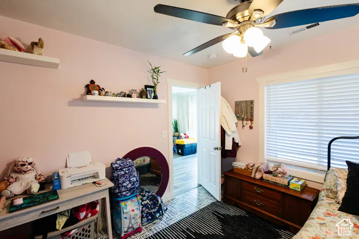Ceiling fan with integrated lighting, window with blinds, wood-finish flooring, two wall-mounted floating shelves
