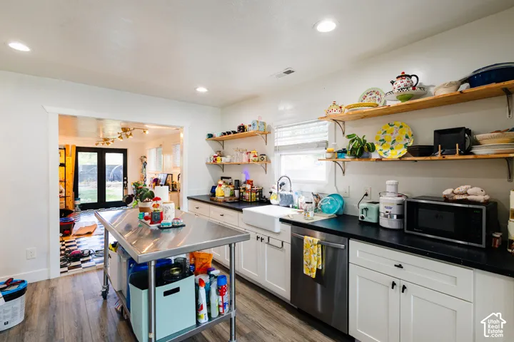 Kitchen featuring white cabinetry, dark countertops, a farmhouse sink, stainless steel dishwasher, and wood-finish flooring