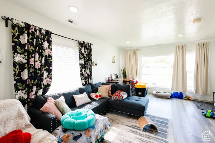 Recessed lighting illuminates the living area, featuring wood-finish flooring and multiple windows