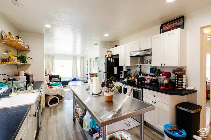 White shaker cabinetry with black hardware, dark countertops, a stainless steel mobile island, and wood-finish flooring