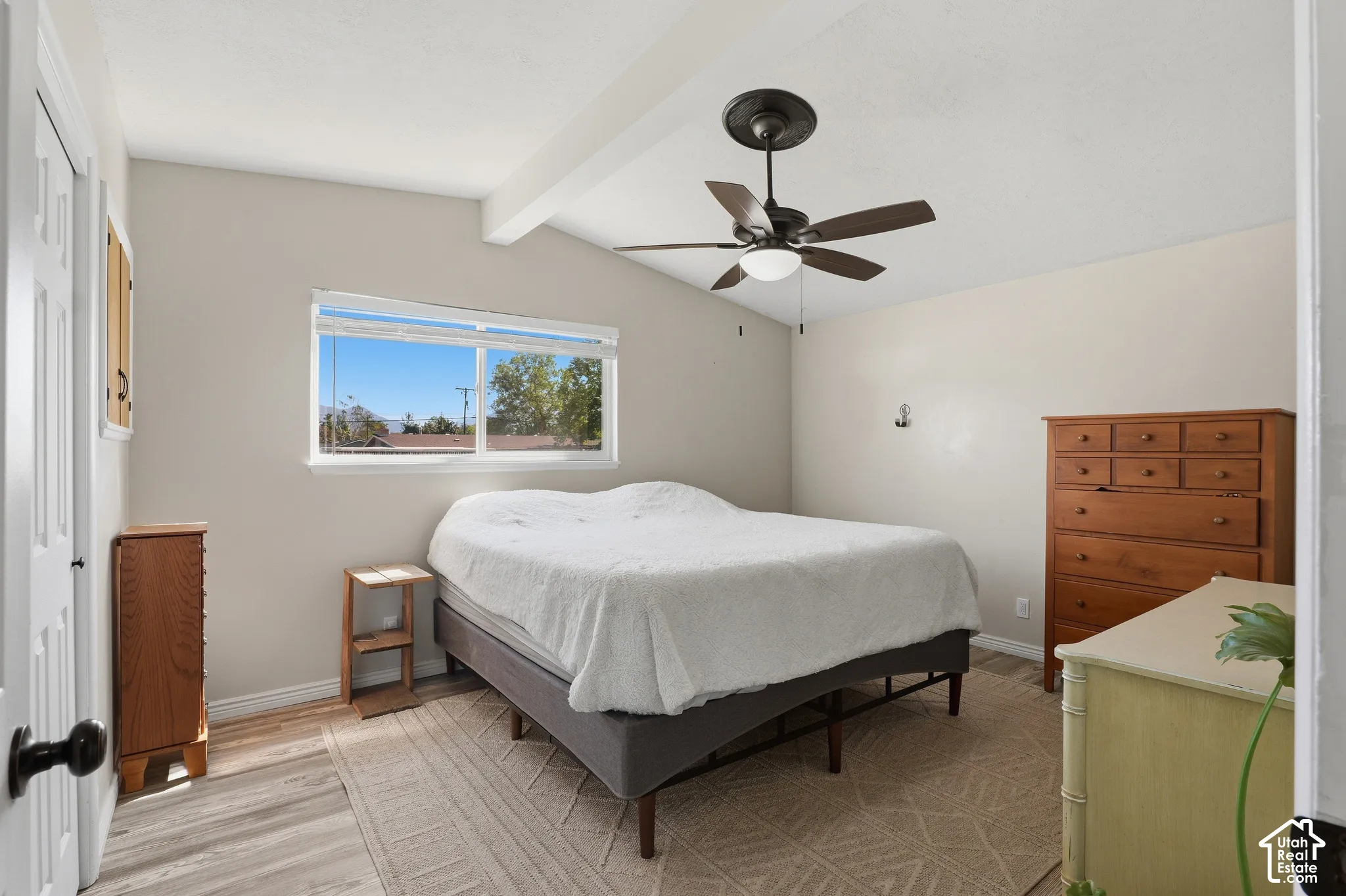 Wood-finish flooring, vaulted ceiling with exposed beam, and a ceiling fan with integrated lighting