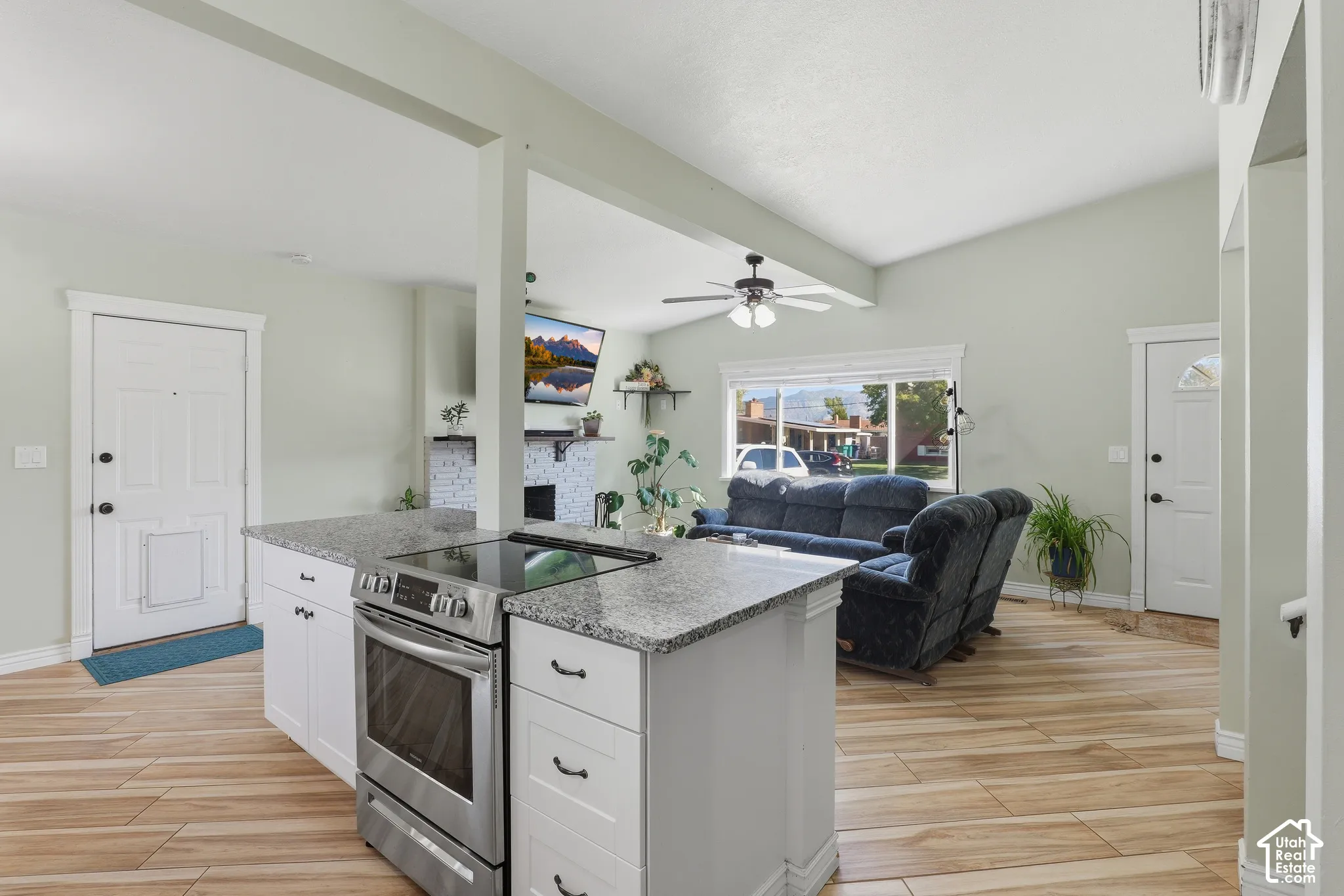 Kitchen island with granite-finish countertop, stainless steel electric range, and white cabinetry