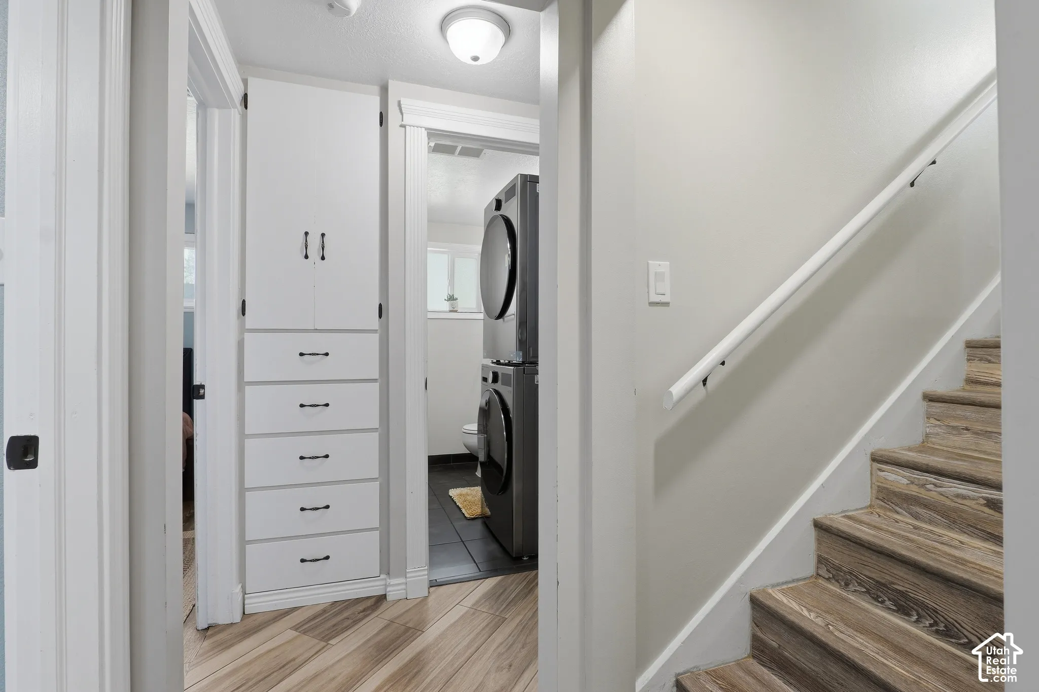 Built-in white cabinetry with drawers, wood-finish flooring, and a white staircase with a handrail