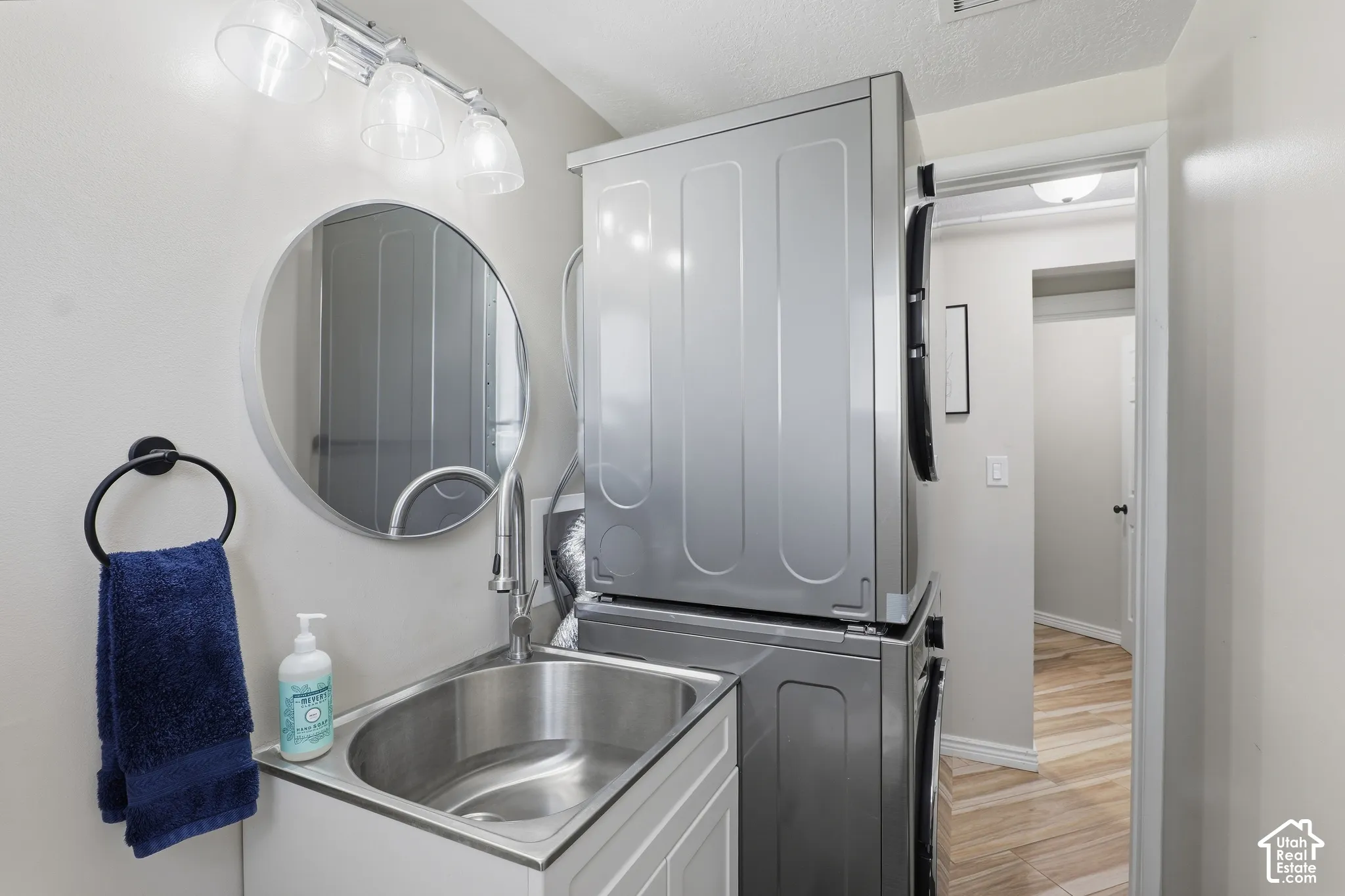 Laundry area featuring a utility sink with a high-arc faucet, a wall-mounted round mirror, and overhead vanity lighting