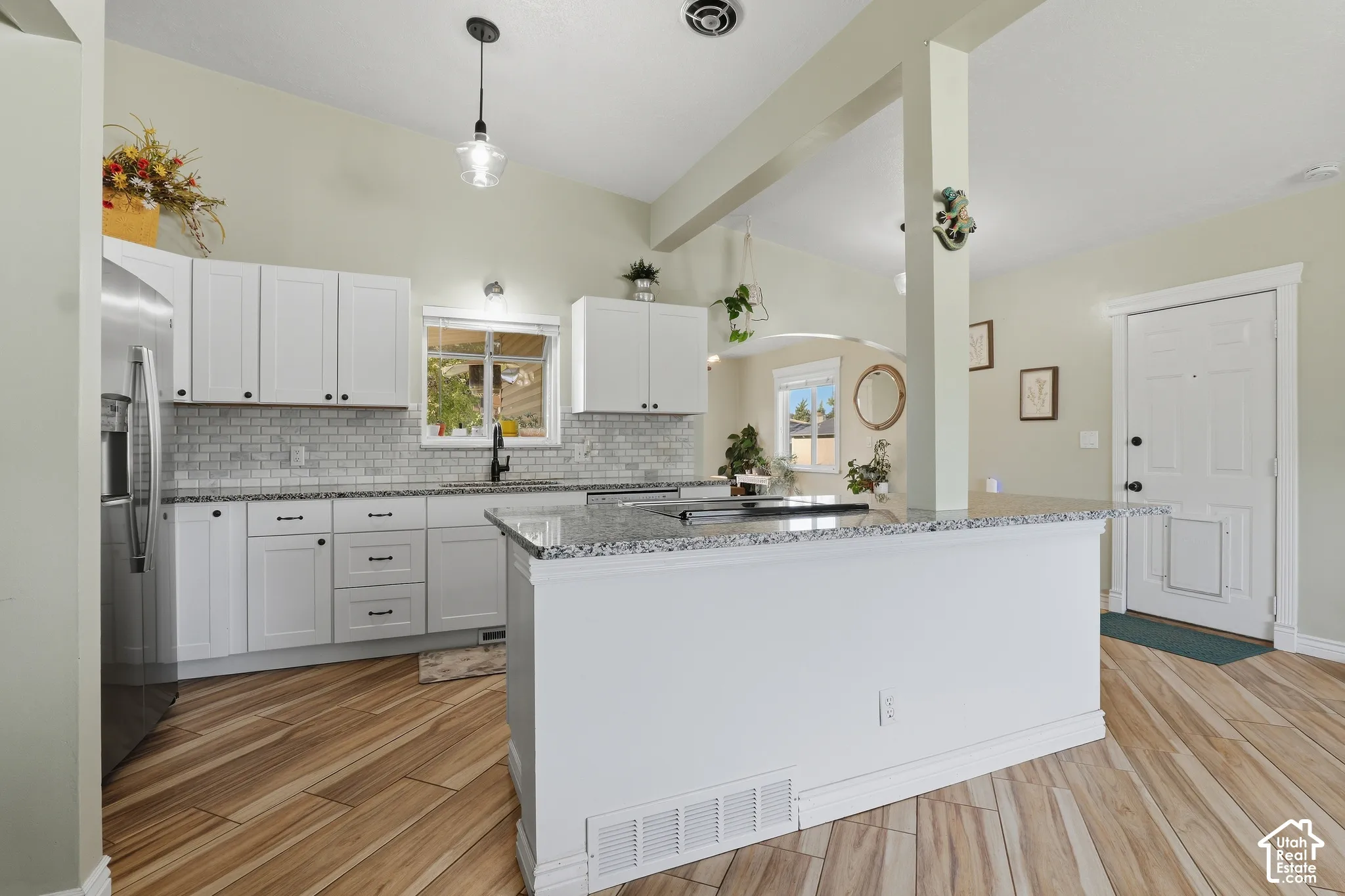 Kitchen featuring wood-finish flooring, white cabinetry, a subway tile backsplash, and a granite-finish island