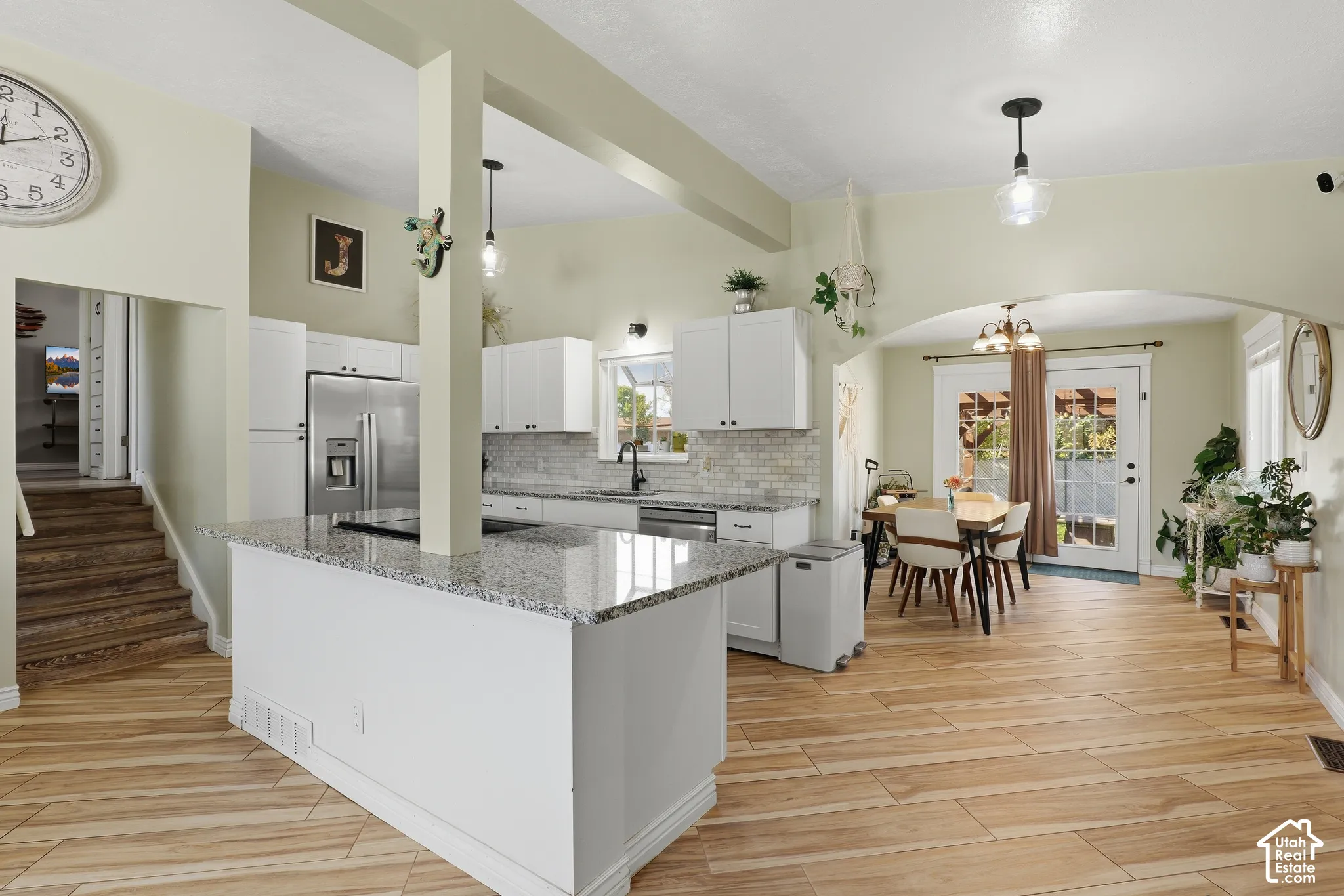 Kitchen island with a granite-style countertop, white cabinetry, stainless steel appliances, and a tile backsplash