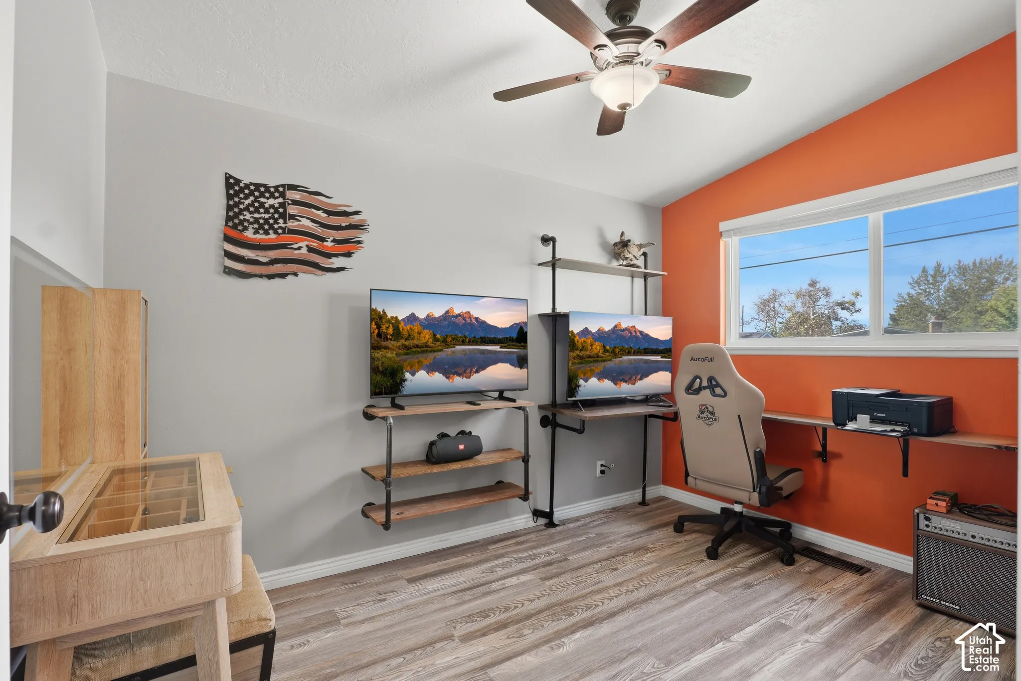 Vaulted ceiling with a ceiling fan, dual windows, wood-finish flooring, and a built-in wall desk with shelving