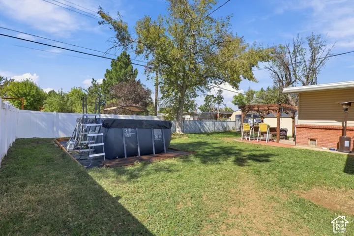 Expansive lawn area featuring a privacy fence, a built-in outdoor pool, and a dedicated patio space with a pergola