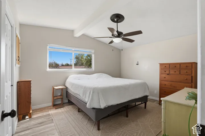 Wood-finish flooring, vaulted ceiling with exposed beam, and a ceiling fan with integrated lighting