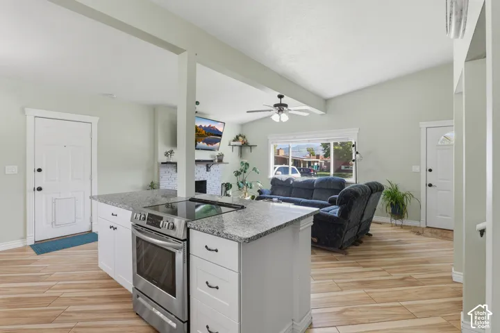 Kitchen island with granite-finish countertop, stainless steel electric range, and white cabinetry