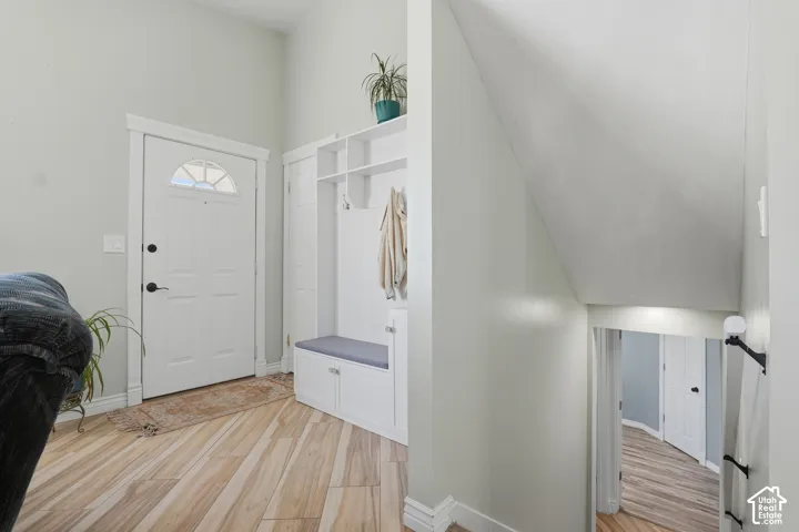 Entryway with wood-finish flooring, a white paneled entry door with an arched window, and built-in white cabinetry with bench seating