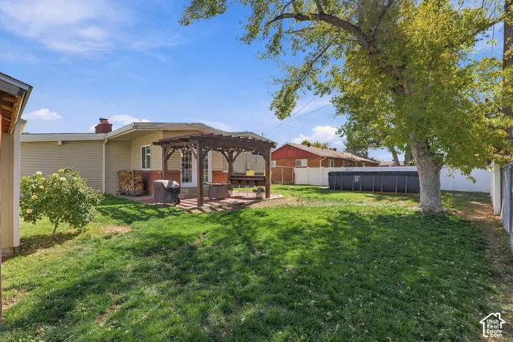 Expansive backyard featuring a manicured lawn, a wooden pergola over a brick patio, mature trees, and a privacy fence