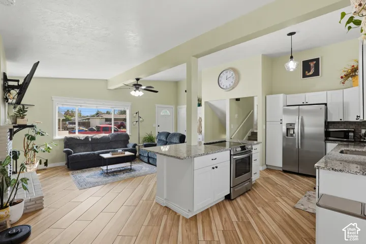 Open-concept living area featuring wood-finish flooring, white cabinetry, stainless steel appliances, and granite countertops