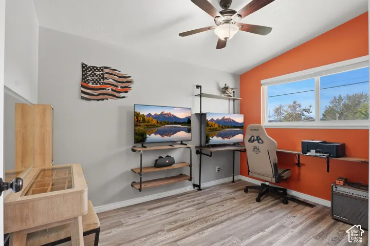 Vaulted ceiling with a ceiling fan, dual windows, wood-finish flooring, and a built-in wall desk with shelving