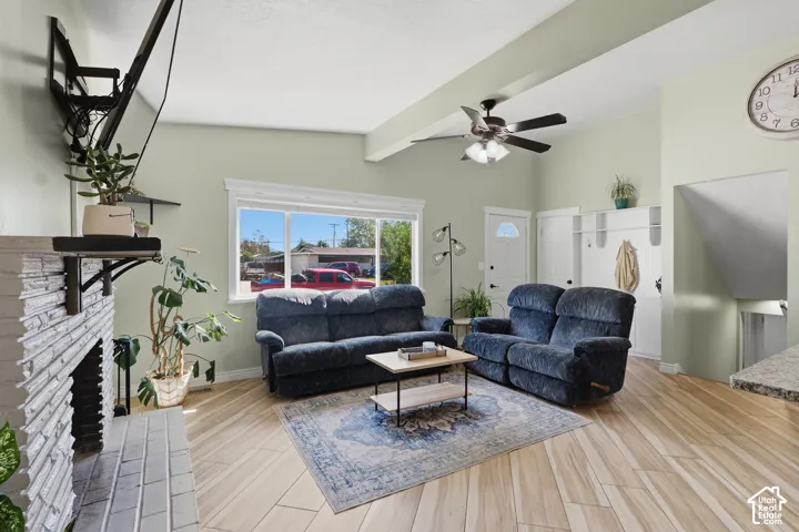 Vaulted ceiling with a ceiling fan, fireplace with a white brick surround, wood-finish flooring, and a built-in storage unit