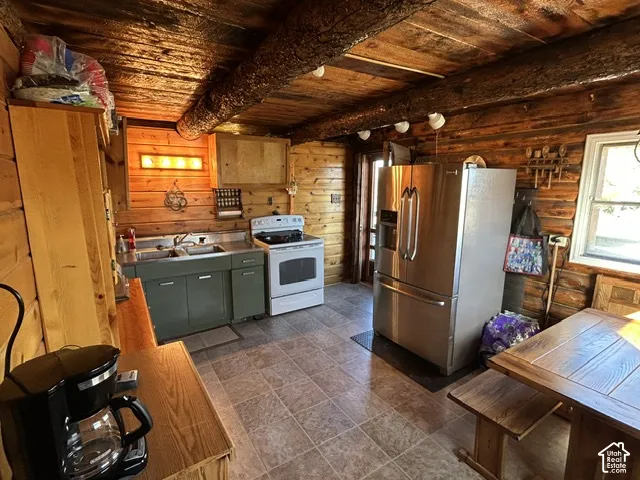 Exposed log beam ceiling, wood-paneled walls, stainless steel refrigerator, white range, and tile flooring