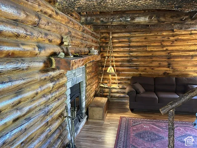 Log-style interior walls, stone fireplace with hearth, wood mantel, wood-finish flooring, and a log stair railing
