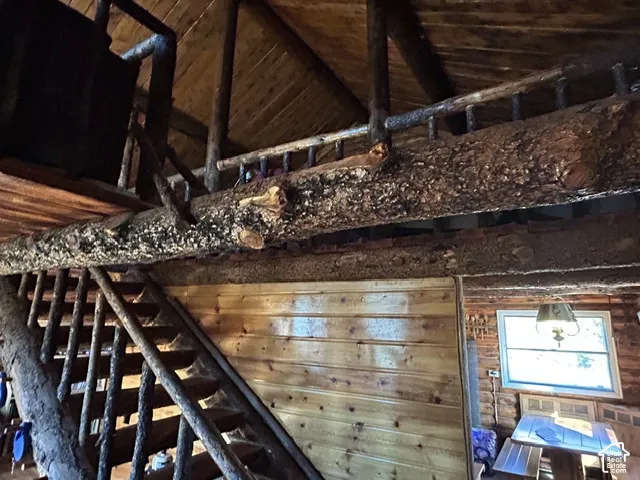 Rough-hewn log structural beams, wood plank ceilings, natural wood staircase, wood plank wall paneling, and an exposed wood structural beam