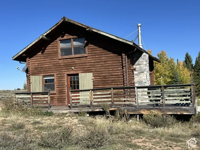 Log cabin exterior featuring a stone chimney, a wooden deck, and a wood-paneled door with shutters