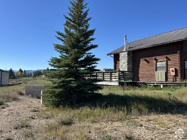Log cabin exterior featuring a metal roof, stone chimney, and an attached wood deck