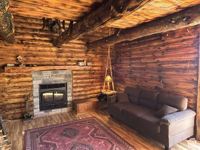Log cabin interior featuring exposed wood beams, wood-finish flooring, and a stone-surround fireplace with a wood mantel