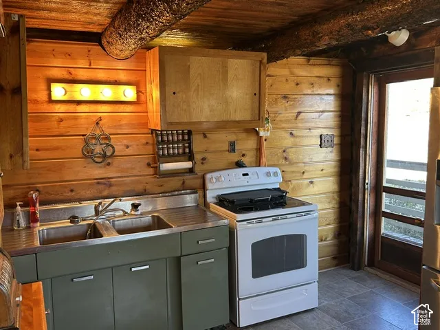 Wood-paneled walls and ceiling, exposed wooden ceiling beams, built-in wooden cabinetry, double basin stainless steel sink, and white freestanding oven
