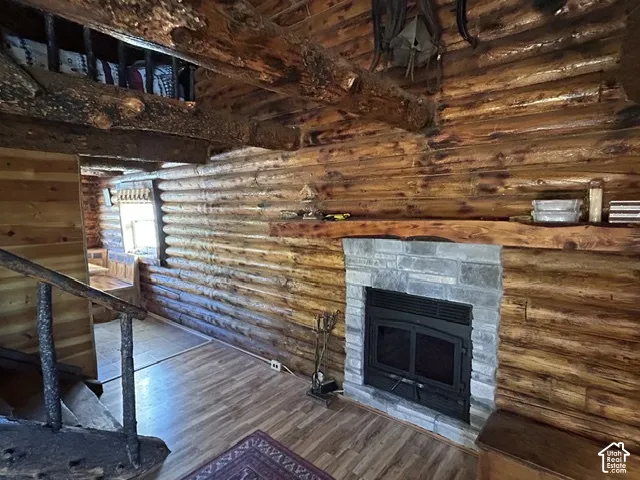Log wall construction with exposed log beams, stone-faced fireplace, wood-finish flooring, and a natural wood staircase