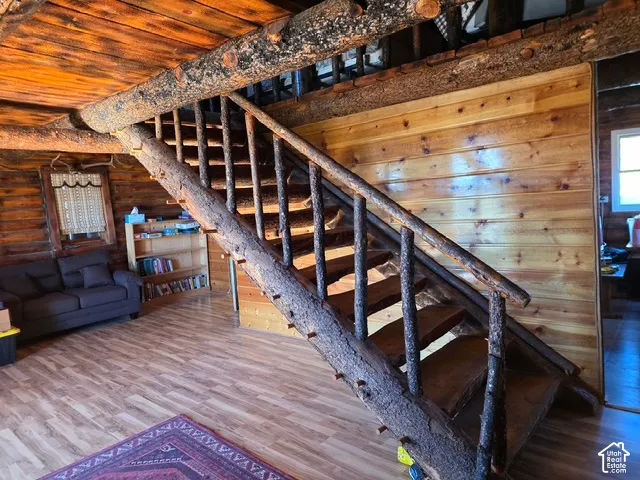 Natural wood staircase with bark-on newel posts and balusters, wood-finish flooring, and horizontal wood paneling