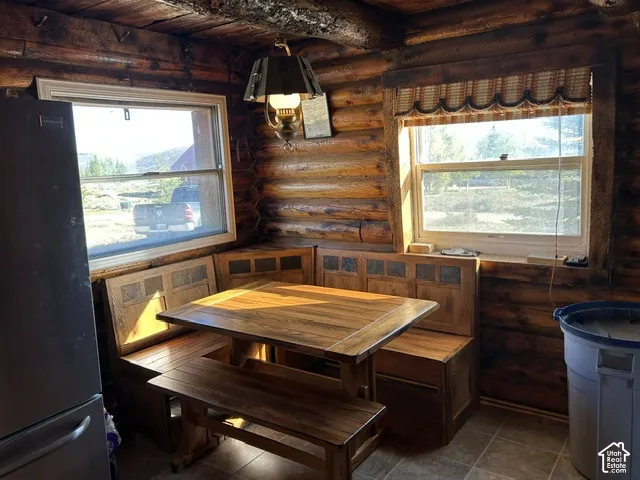 Log construction walls, built-in wood dining nook, wood-finish flooring, two windows, and rustic wall-mounted light fixture