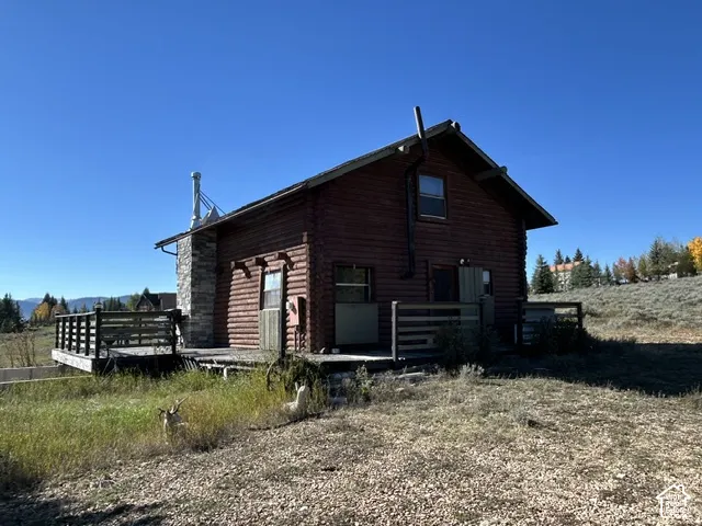 Rustic log cabin exterior with a stone chimney, an expansive wooden deck, and an upper-level window