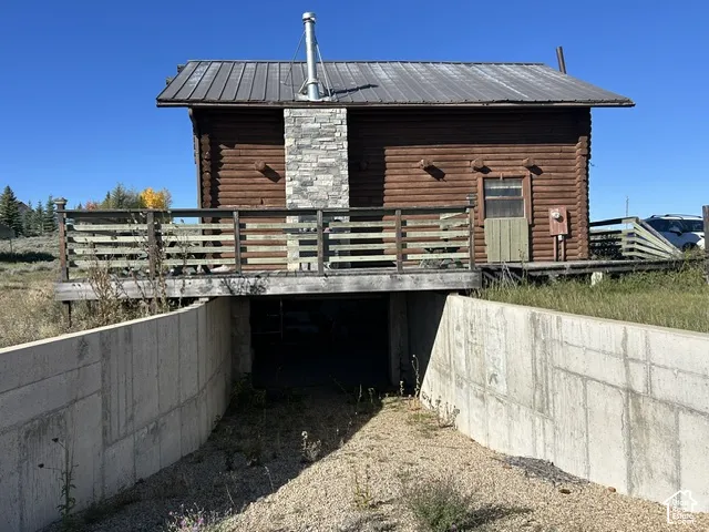 Log-style exterior with a metal roof, prominent stone chimney, and an elevated wooden deck