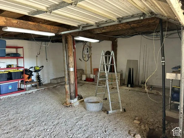 Gravel flooring with exposed wood beam ceiling, white walls, and fluorescent lighting