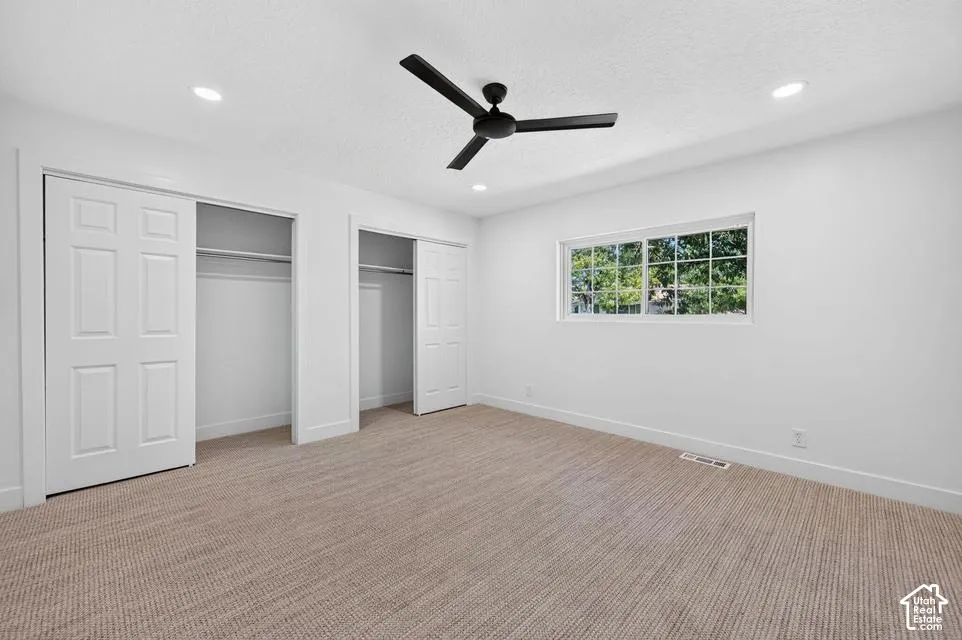 Recessed lighting, ceiling fan, window with exterior scenery, two closets with sliding paneled doors, and neutral carpeting