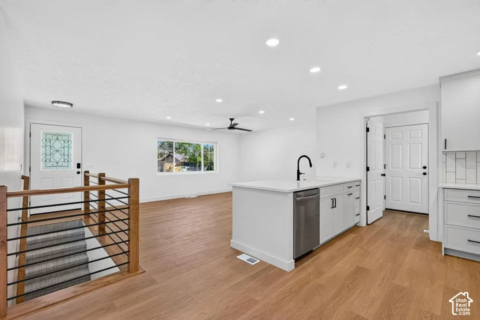 Open-concept living space with wood-finish flooring, white cabinetry, a kitchen island with an integrated sink, and recessed lighting