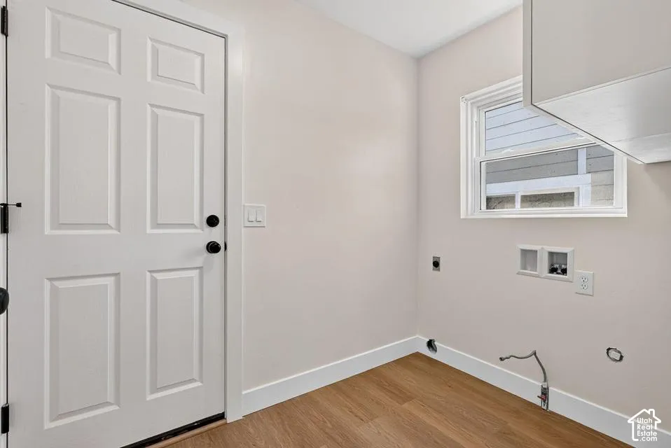 Light-toned wood-finish flooring, white paneled door with black hardware, white trim, and a white framed window