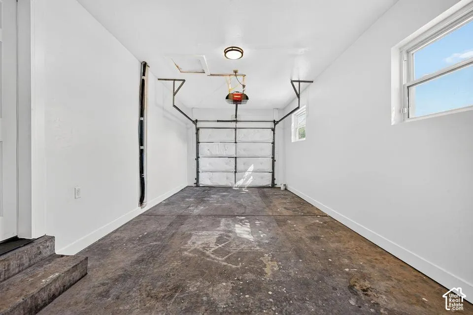 Single-car garage with a roll-up door, exposed concrete flooring, and a ceiling-mounted light fixture