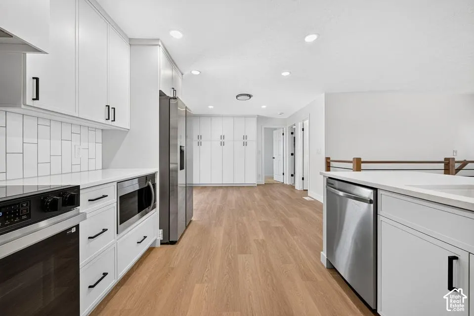 White shaker cabinetry with black hardware, stainless steel appliances, white subway tile backsplash, and wood-finish flooring