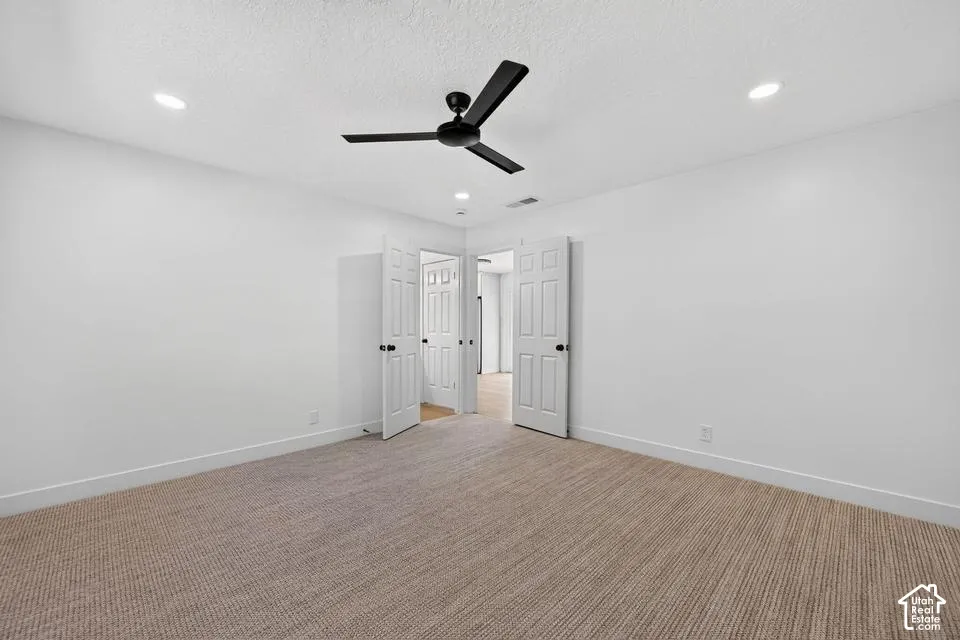 Recessed ceiling lighting, textured carpeting, crisp white walls, and a black ceiling fan