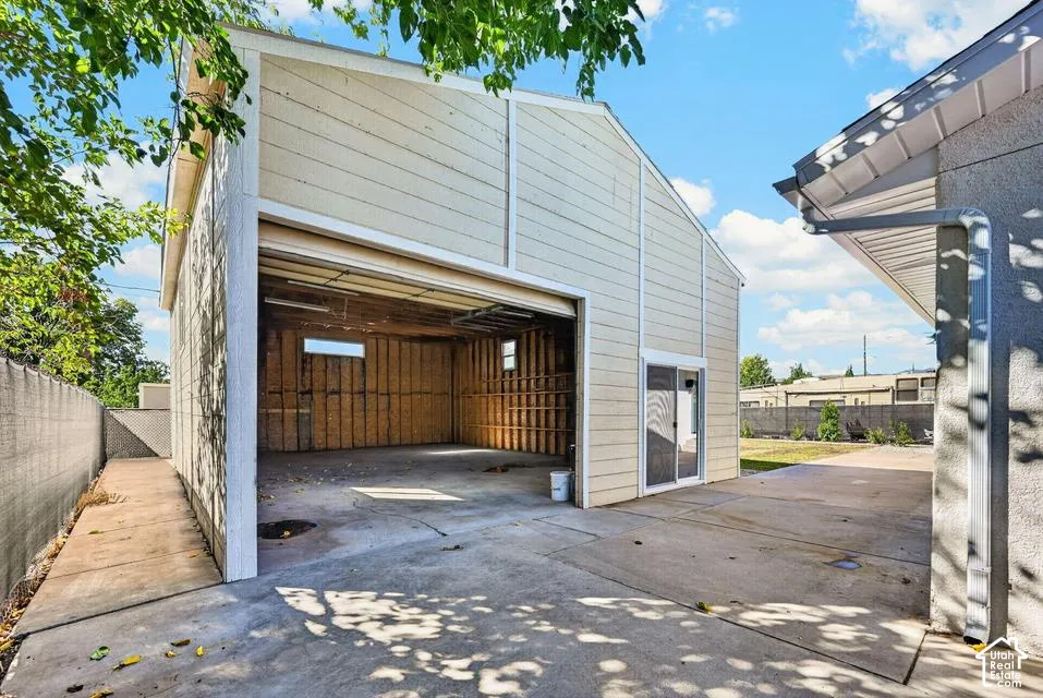 Detached outbuilding with an open garage door, horizontal panel siding, and a sliding glass entry door