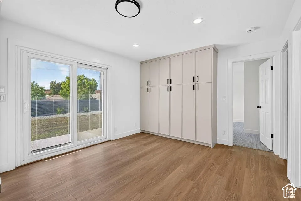 Wood-finish flooring, built-in cabinetry with metal hardware, white sliding glass doors, recessed lighting, and a contemporary flush-mount ceiling fixture