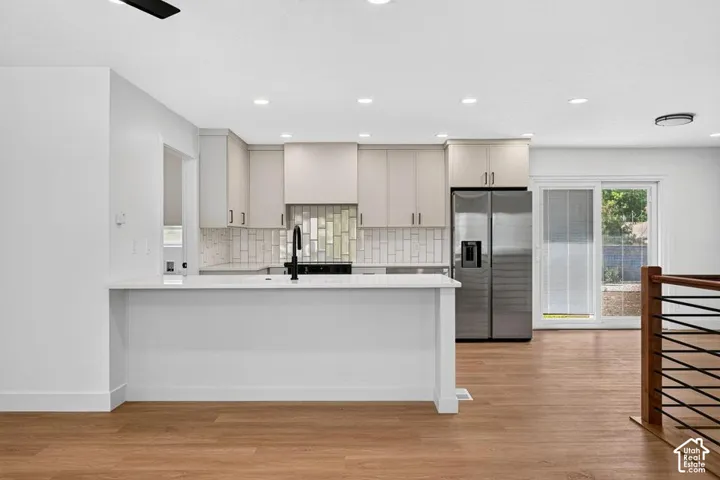 Modern kitchen with light-colored cabinetry, stainless steel refrigerator, white subway tile backsplash, and wood-finish flooring
