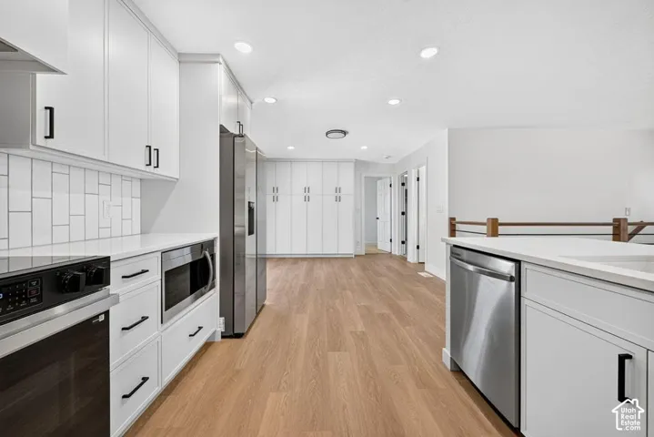 White shaker cabinetry with black hardware, stainless steel appliances, white subway tile backsplash, and wood-finish flooring