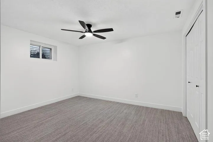 Neutral white walls, textured gray carpeting, and a modern ceiling fan with lighting