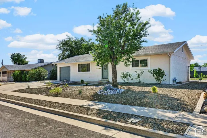Stucco exterior with an attached garage, landscaped front yard with a mature tree, and a concrete driveway