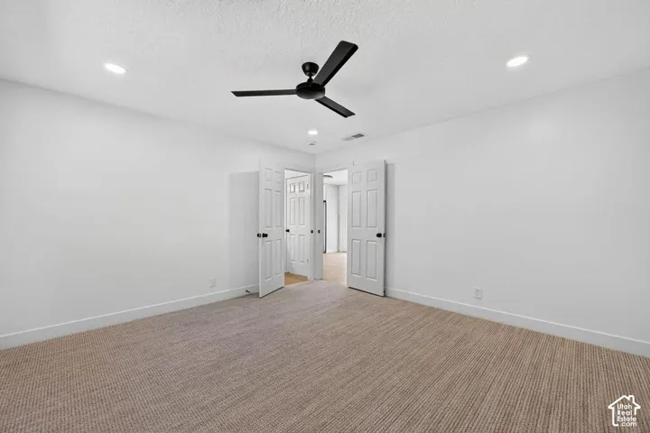 Recessed ceiling lighting, textured carpeting, crisp white walls, and a black ceiling fan