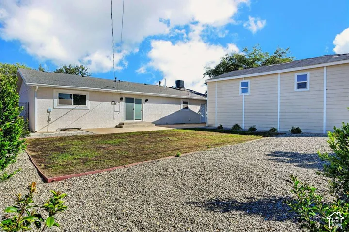 Expansive gravel yard with a grass patch, featuring a stucco-finish exterior, concrete patio, and sliding glass door