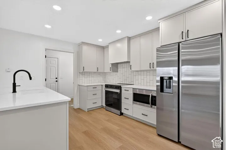 Kitchen featuring light wood-finish flooring, white cabinetry with black hardware, stainless steel appliances, a white subway tile backsplash, and recessed ceiling lighting
